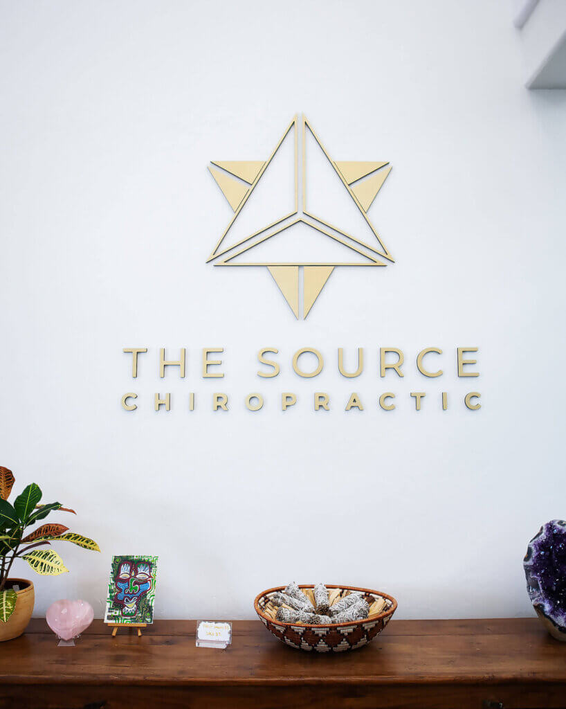 A sign that says The Source Chiropractic with their logo, a two triangles overlapping, hanging over the reception desk