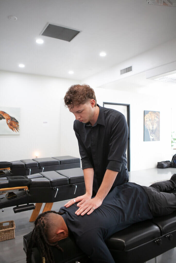 A caregiver performing an adjustment on the back of a patient lying facedown on a table at the chiropractic adjustment clinic